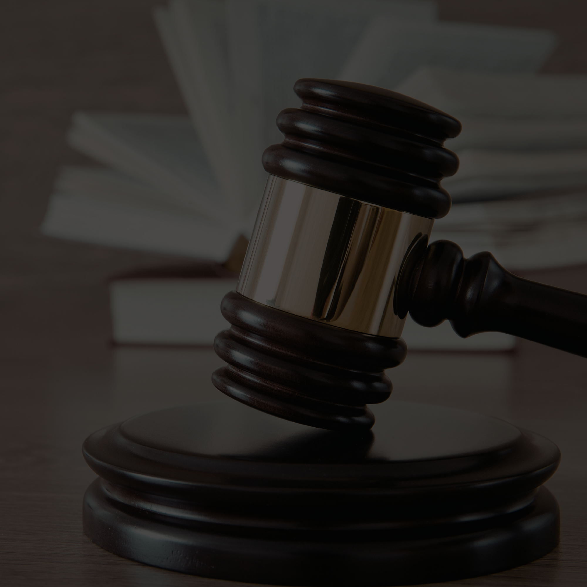 A wooden gavel rests on a wooden base, with a stack of books in the background.