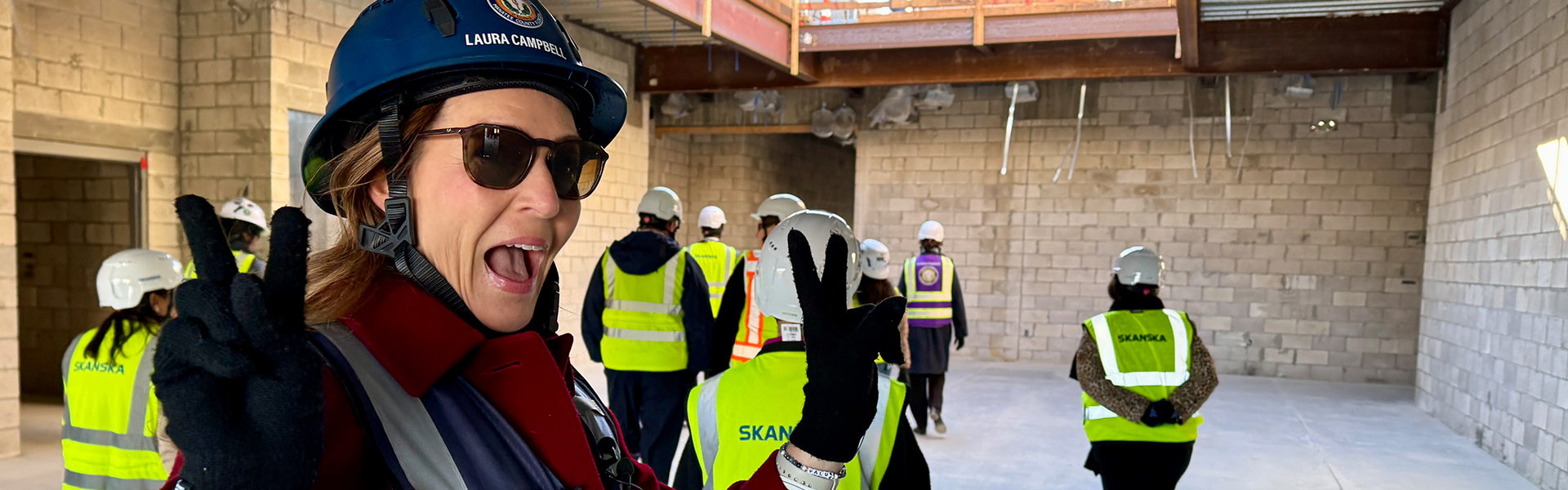 Principal Campbell smiles while wearing a hardhat and reflective vest as she walks through the construction site.