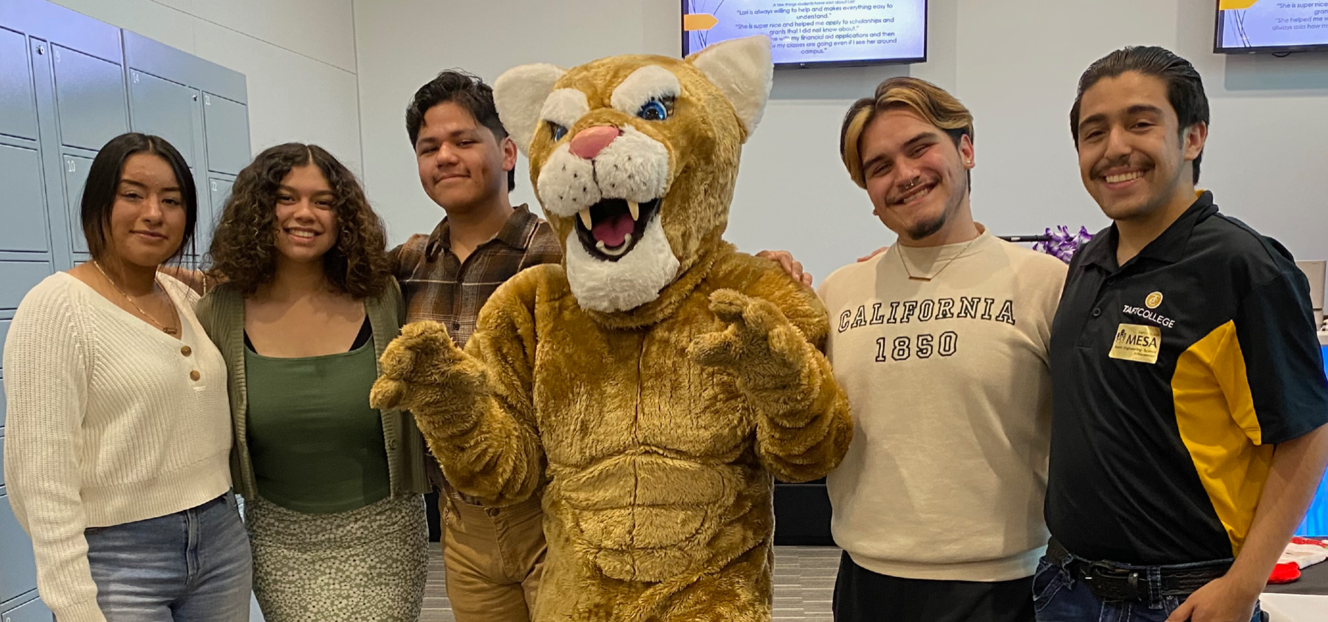 A group of five individuals, one in a tiger mascot costume, standing together in a room.