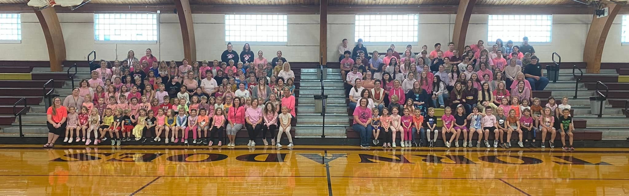 picture of staff  and students sitting on the bleachers and smiling at the gym