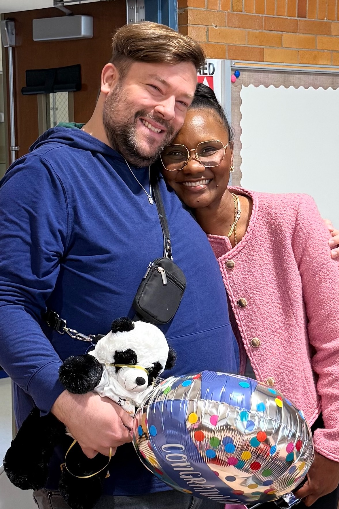 Man and woman smiling with one holding a stuffed panda and a balloon, and the other with glasses.