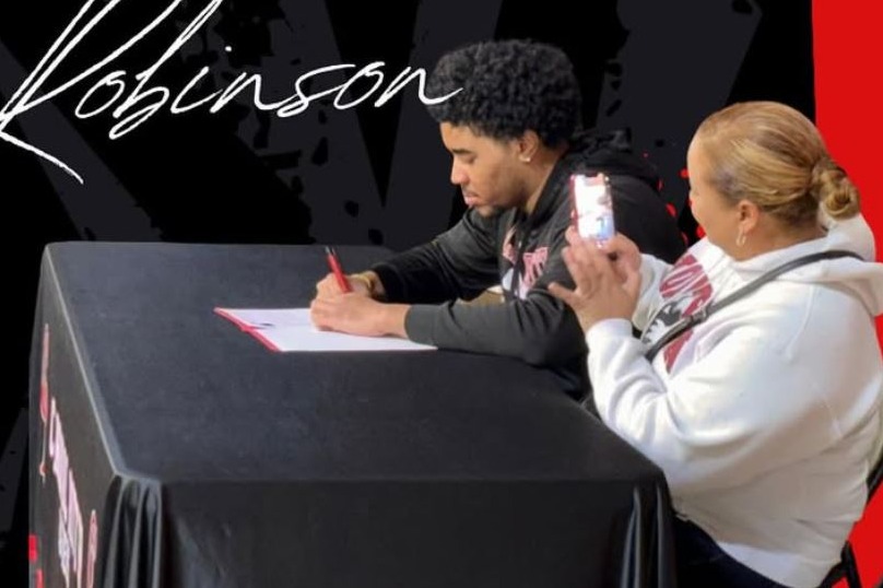 Poster with "SIGNED" in bold red letters. A person signs paper while another watches. "Northern Illinois University" and "NIU Huskies" on the poster.