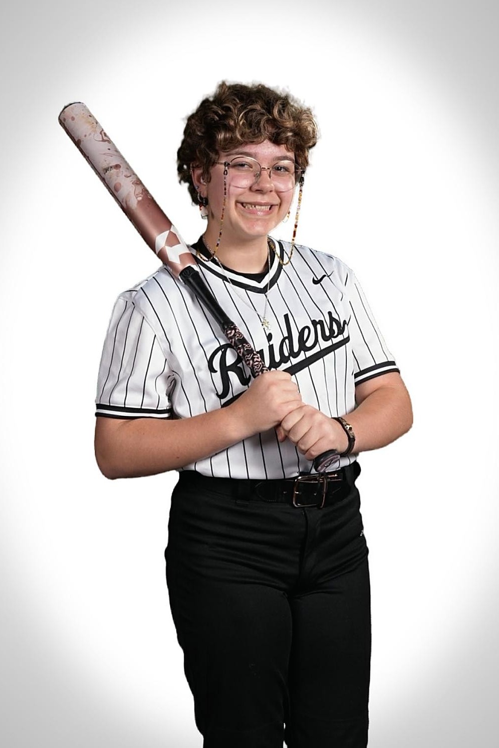 A person with short hair wearing a Raiders jersey and glasses holds a baseball bat.