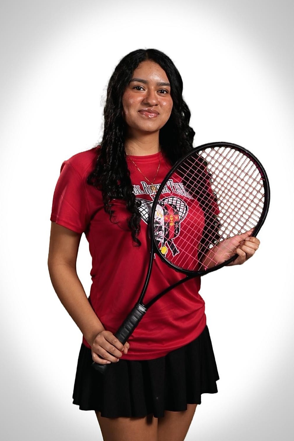 Woman in red shirt and black skirt holding tennis racket against a white background.