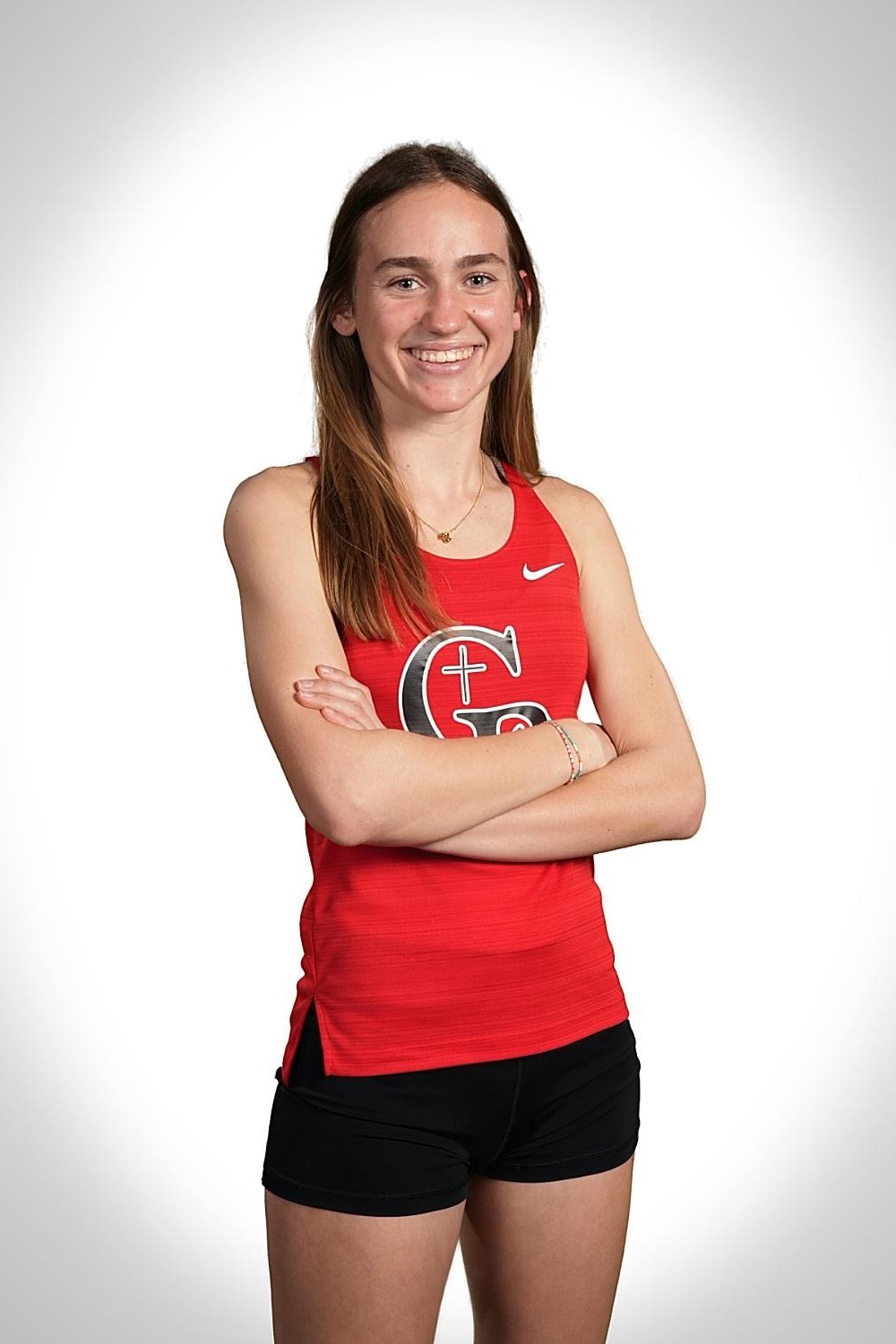 Woman in red tank top with white lettering, black shorts, and a necklace poses for a photo.