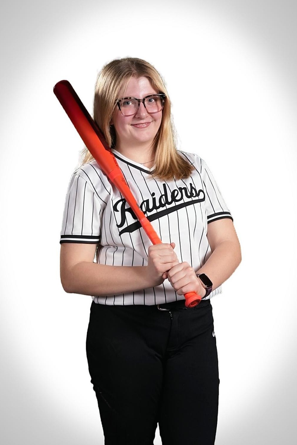 Woman wearing glasses, a Raiders jersey, and black pants holds a red baseball bat.