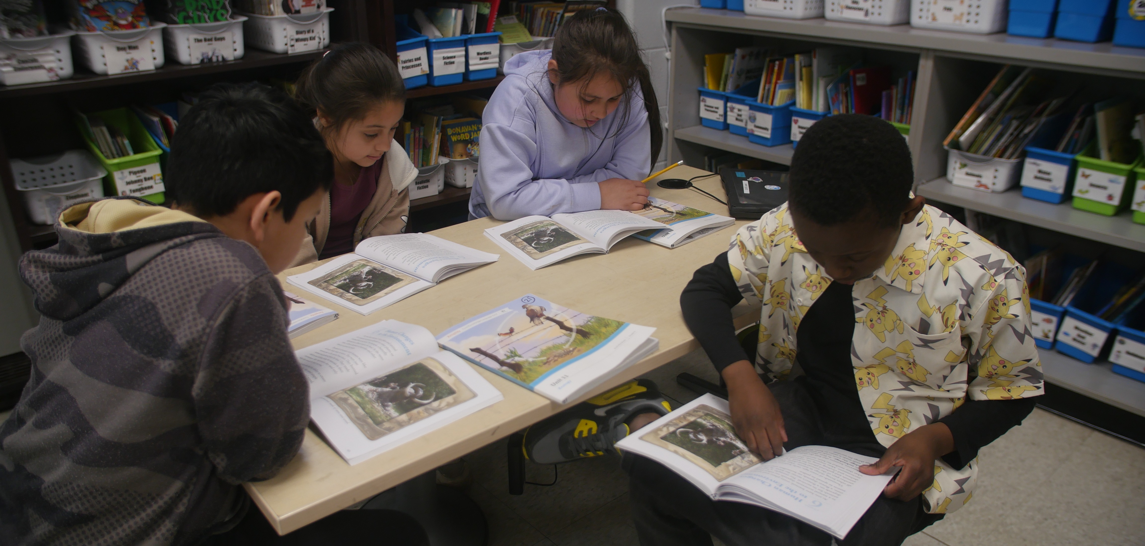 Four students sit together at a table, focused on reading books.
