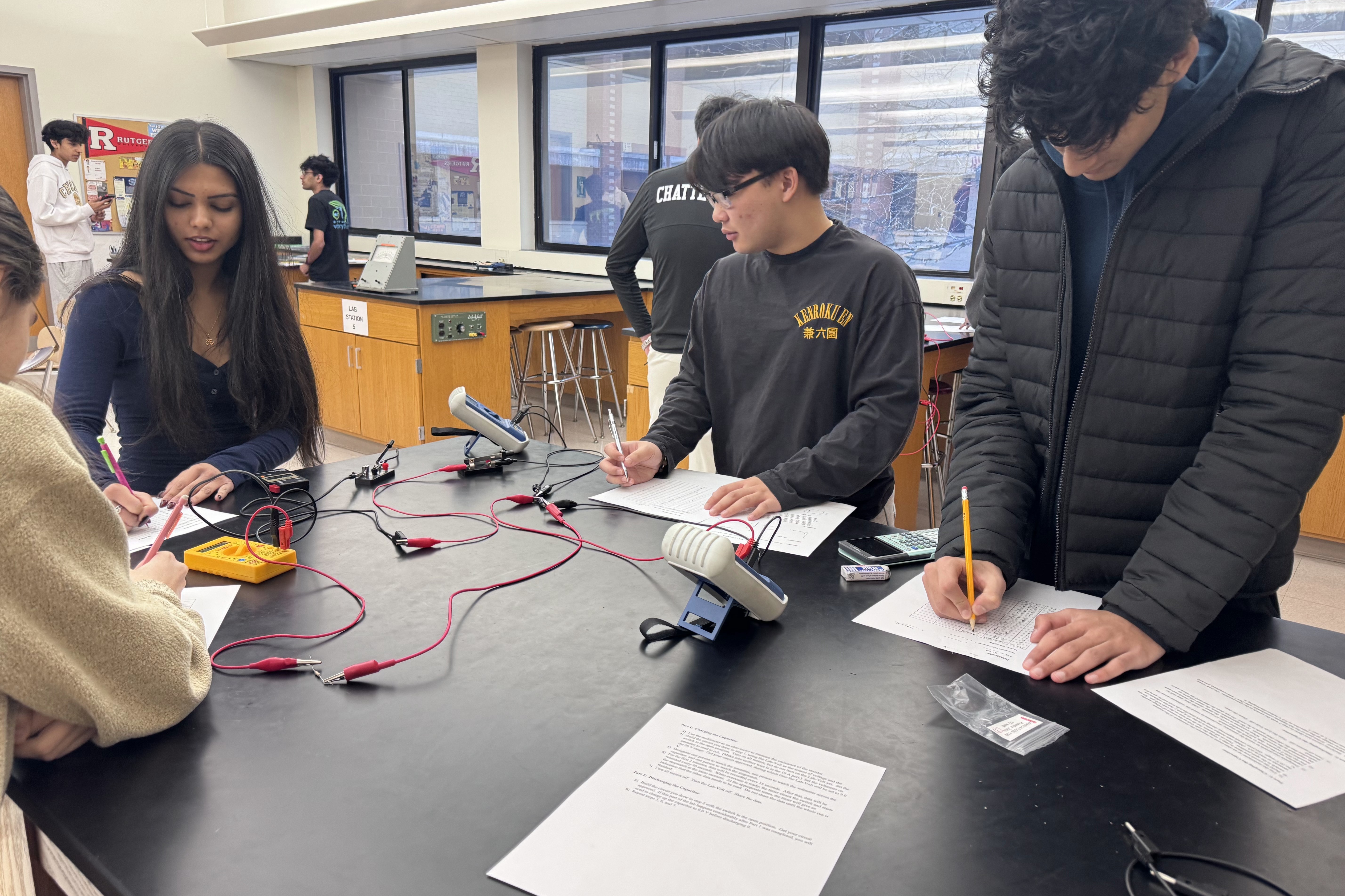 A group of people in a lab, writing on papers while working on a project.