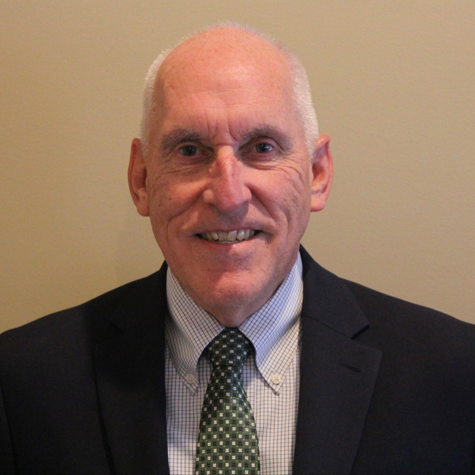 Older man with white hair wearing black suit and green tie, smiling and looking at the camera.