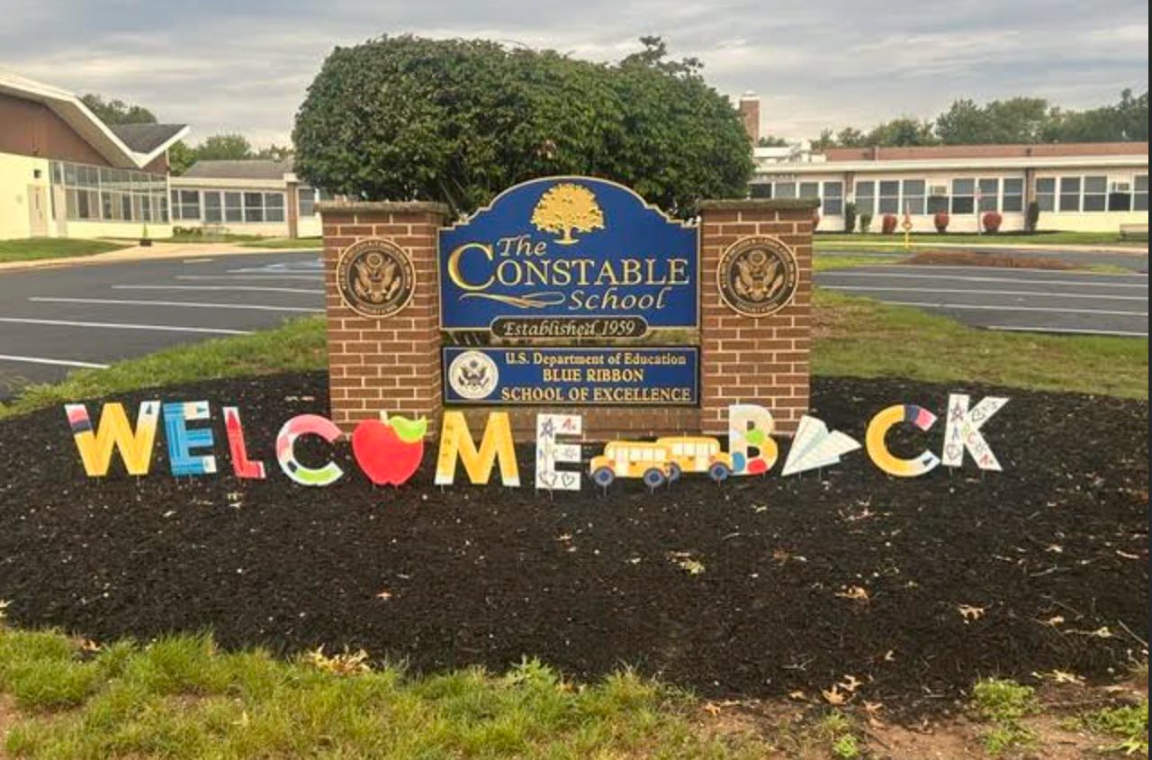 A sign reading "The Constable Academy" in front of a school. Colorful letters spell "Welcome Back" on mulch.