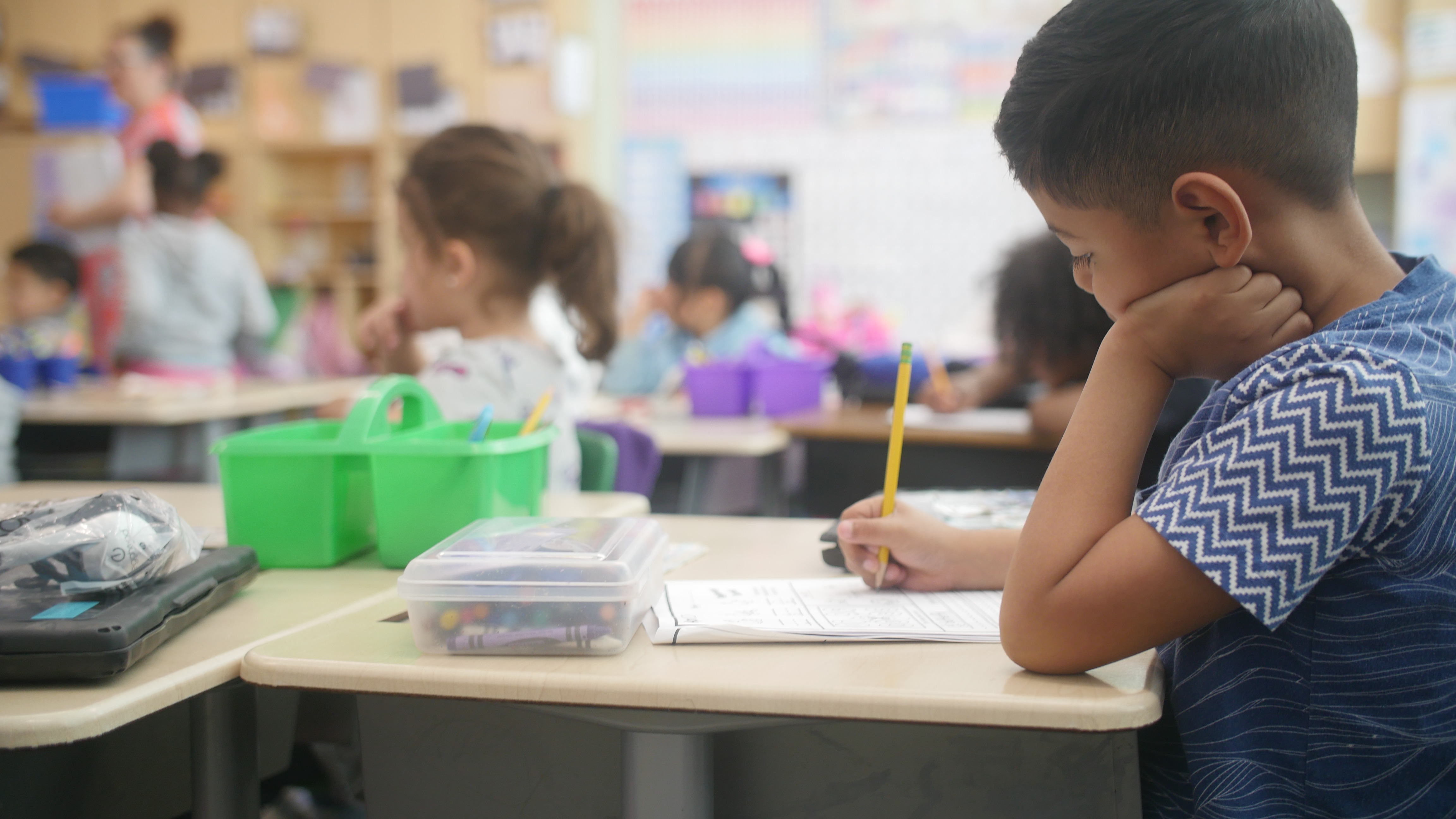 Student sit at his desks, holding a pencil and focused on working through their classroom worksheets