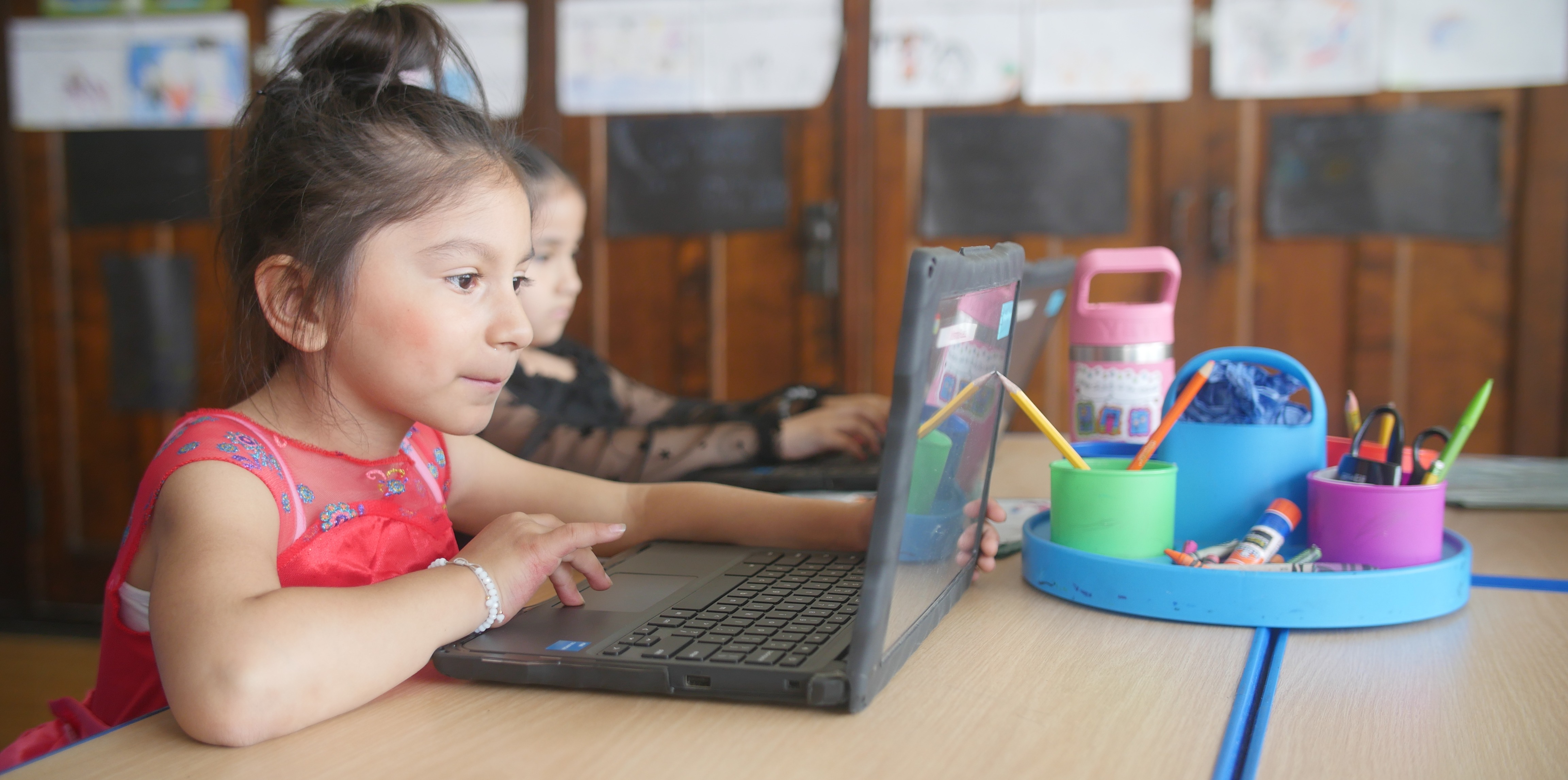 Two students seated at their desks, actively engaged in a digital lesson on their Chromebook laptops