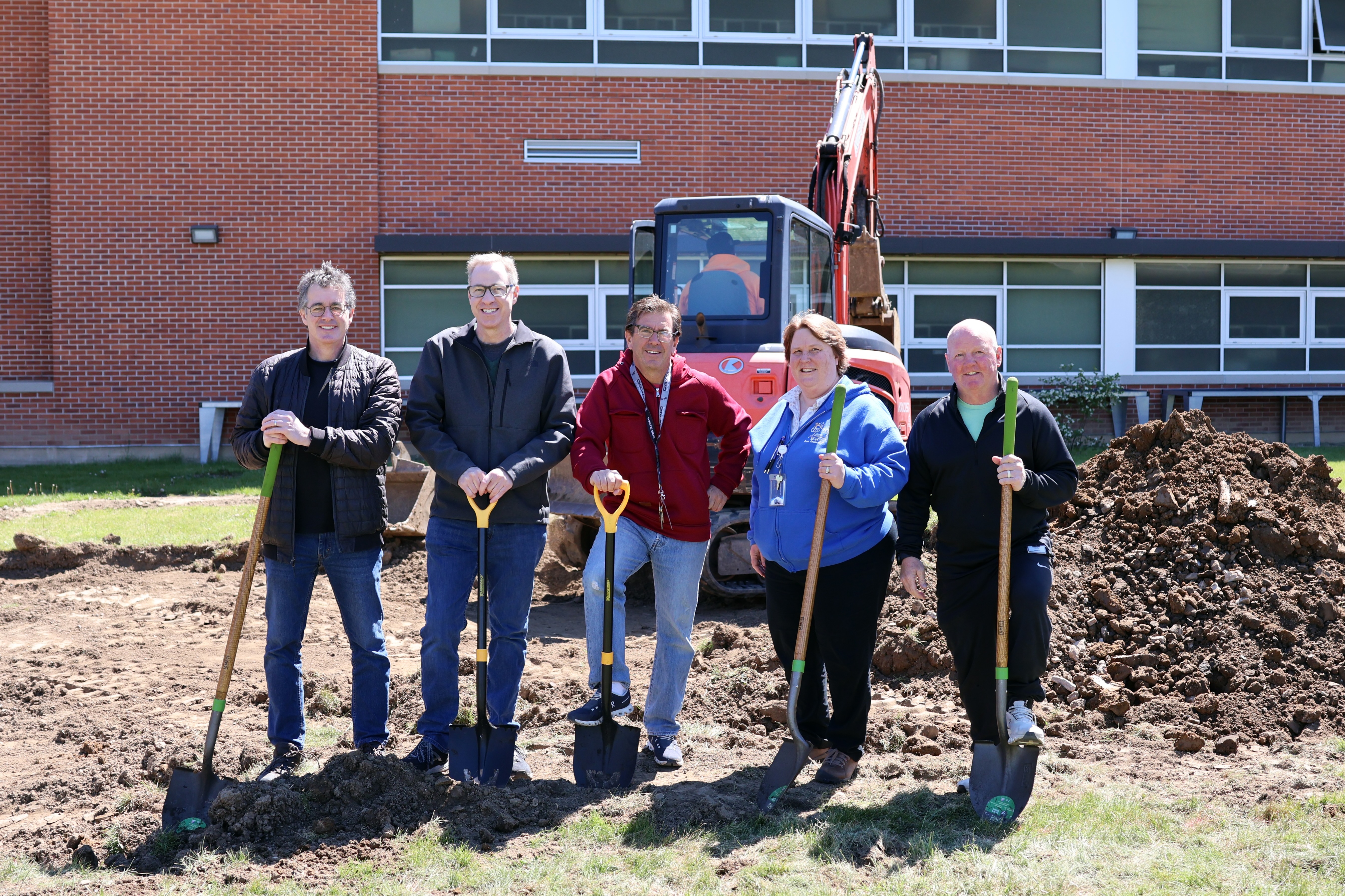 Five school staff members stand together holding shovels during a groundbreaking ceremony.