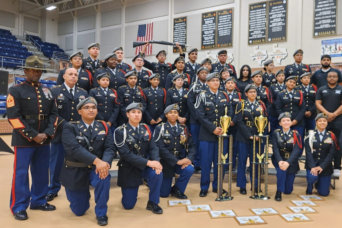A group photo of JROTC cadets smiling in their full dress uniforms, proudly holding up and displaying the trophies they won at a competition