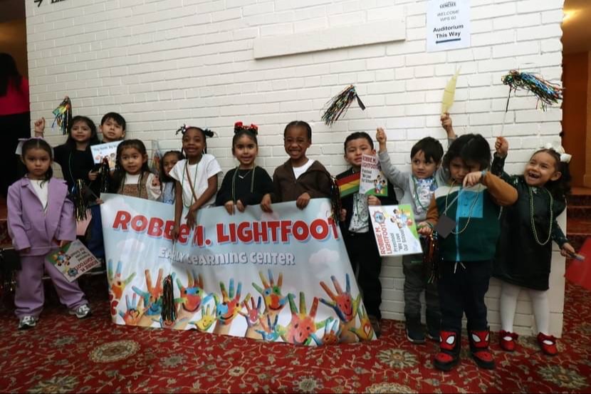 Smiling Pre-K students holding up a banner that reads 'Robbie M. Lightfoot'.