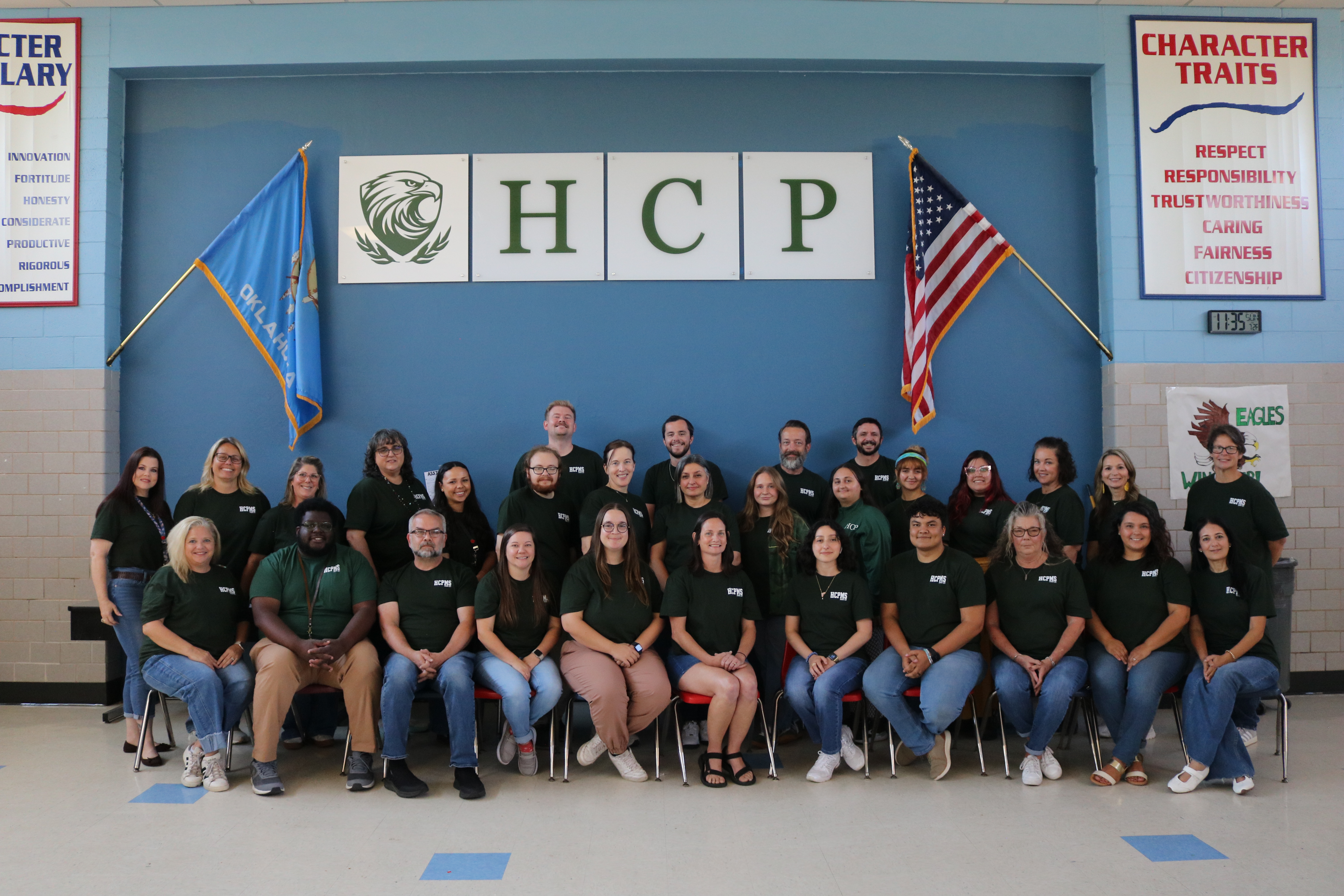 Group photo of people in green shirts sitting in rows, with a blue wall behind them.