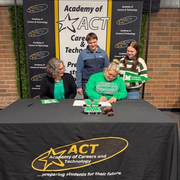 Academy of Careers and Technology student Bella Kincaid, accompanied by a college representative, signs a letter of intent to attend Marshall University while friends look on.
