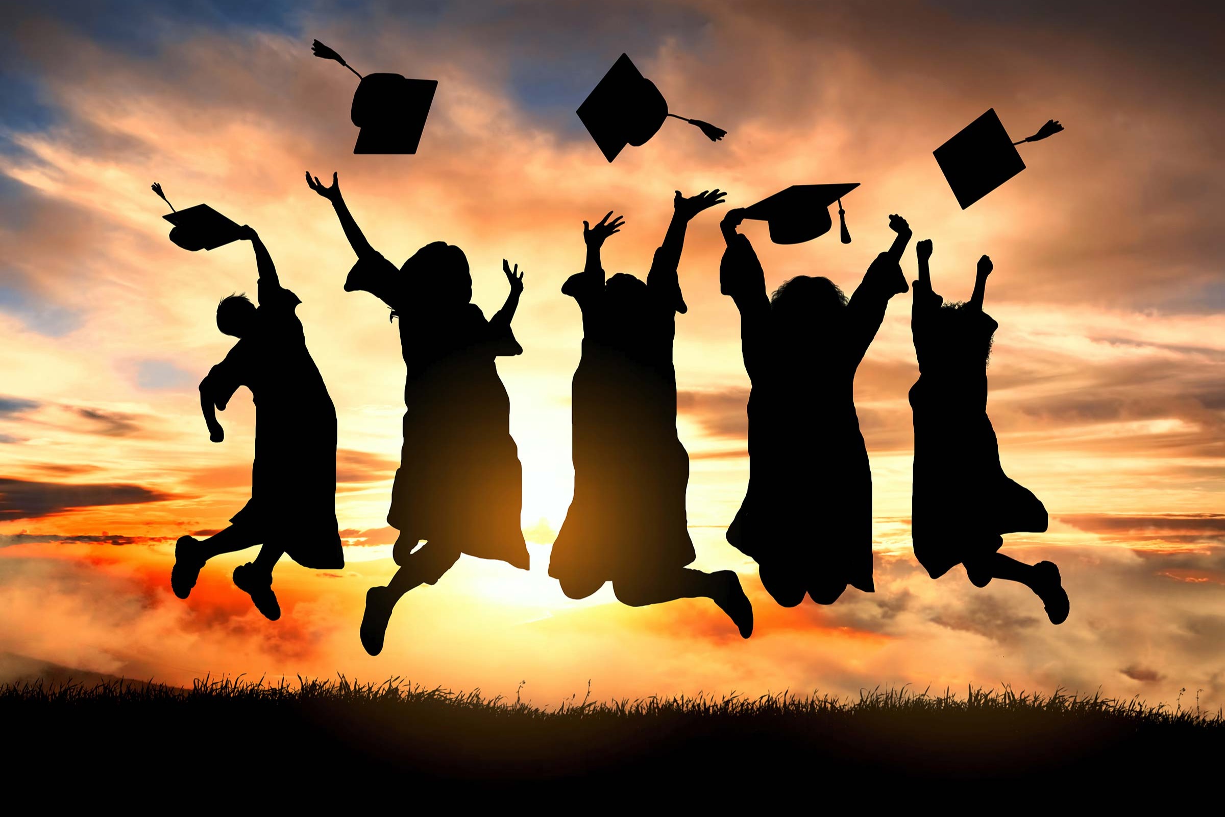 Five people jump in the air, throwing graduation caps into the sky. Sunset behind them.