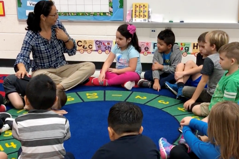 A dual language teacher sitting in a circle on the floor with her students