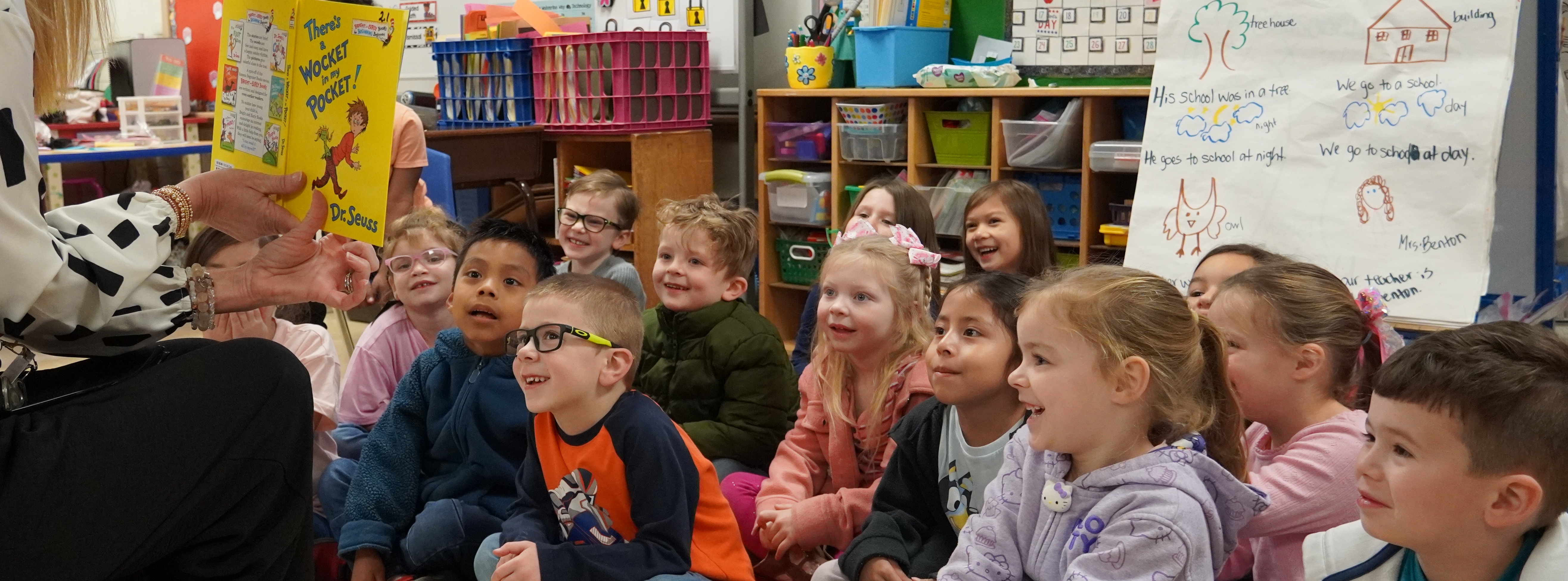 students sitting on the floor while a book is read to them