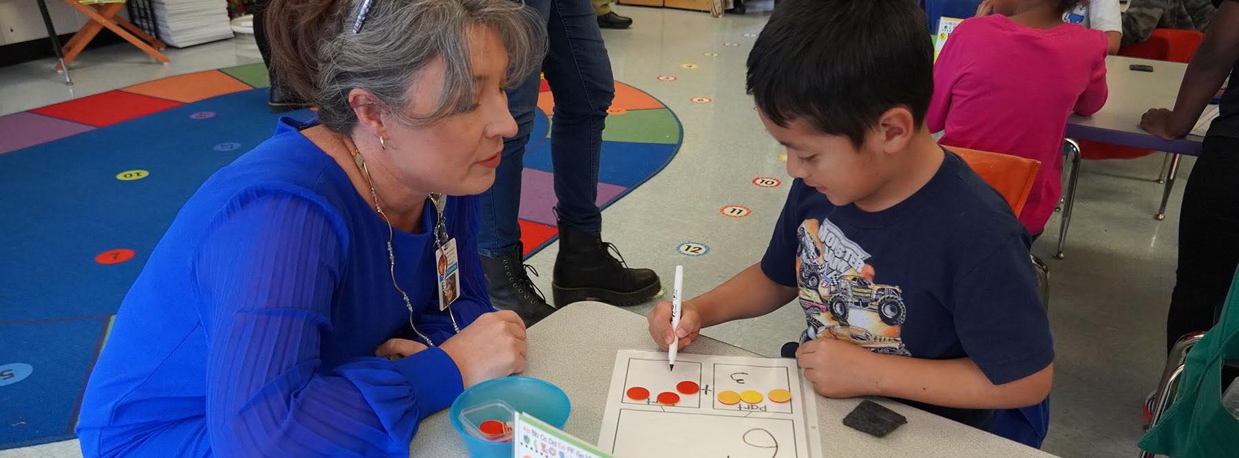 principal helping student with a math worksheet at a desk
