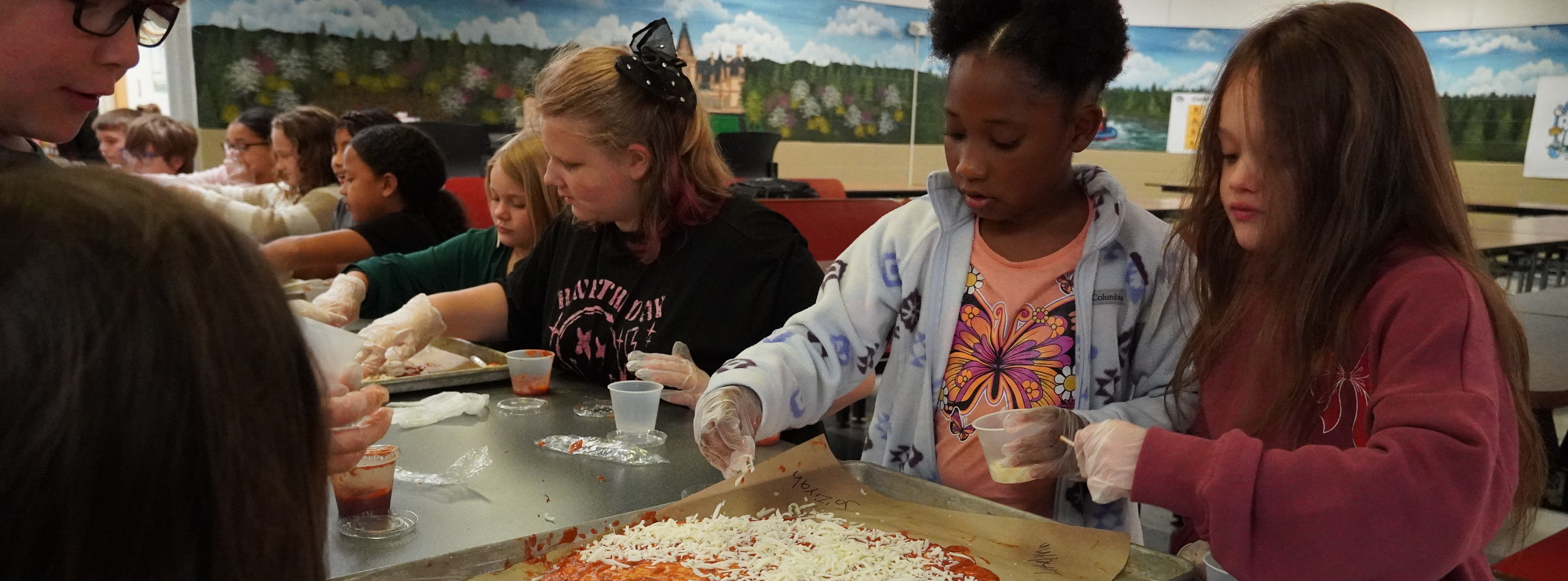 students putting cheese on a pizza