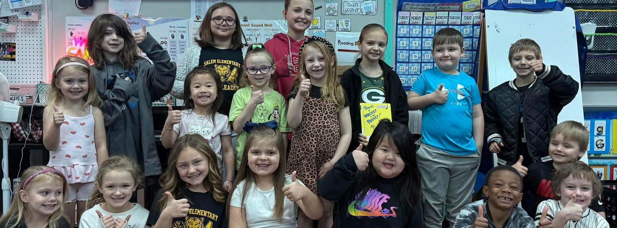 students standing in a group with thumbs up and books