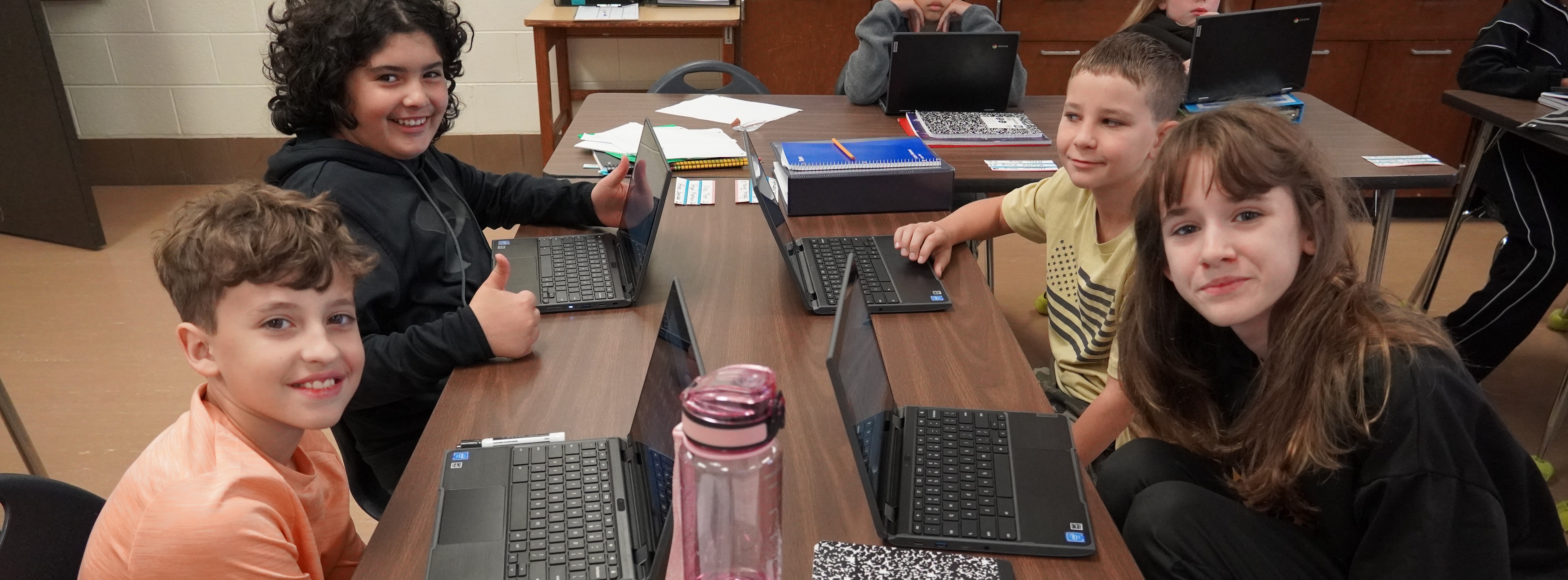 students at a table smiling with laptops