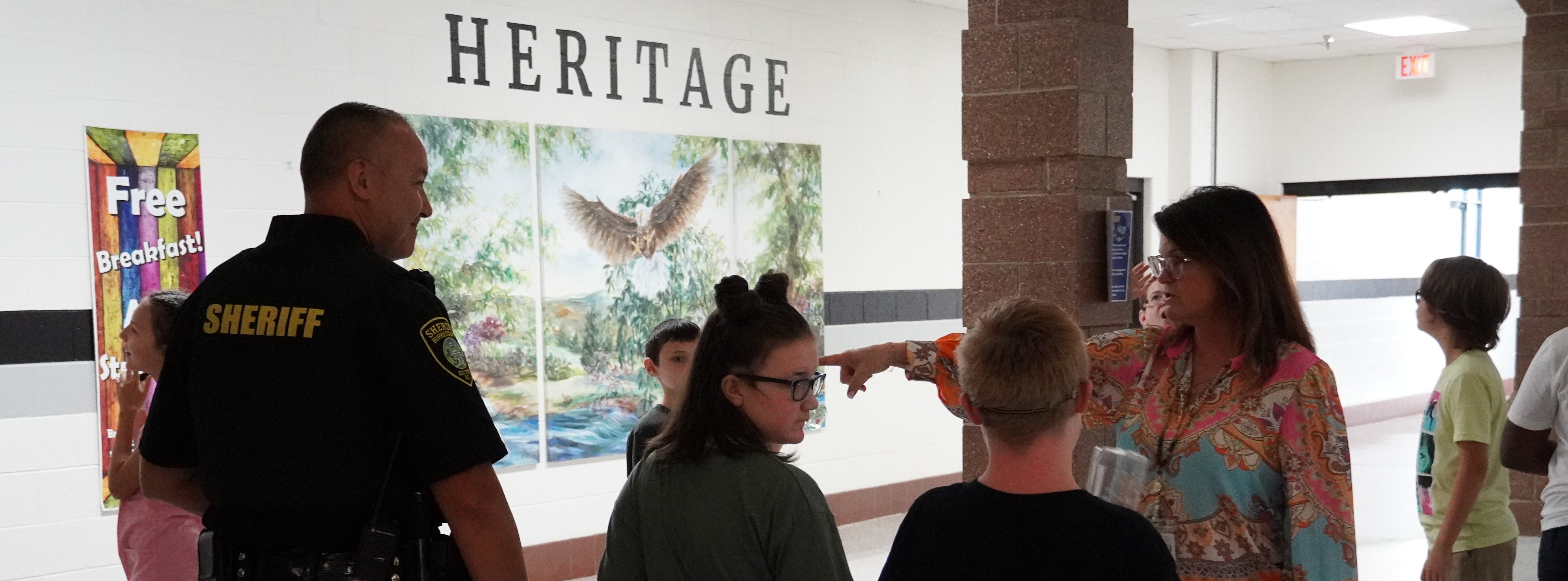 student holding hands with school resource officer. wall behind them says Heritage with an eagle painting