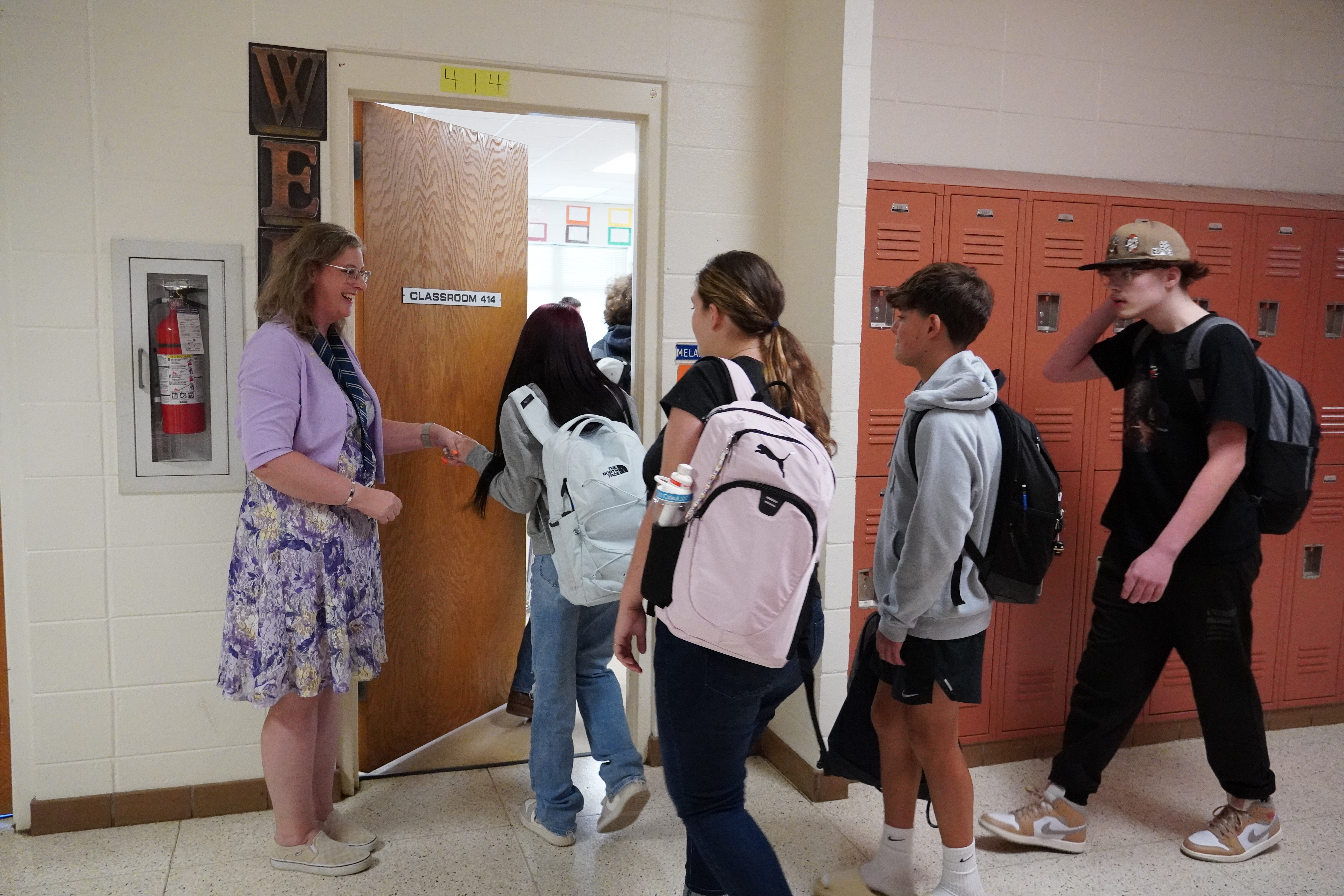 students entering classroom greeted by teacher