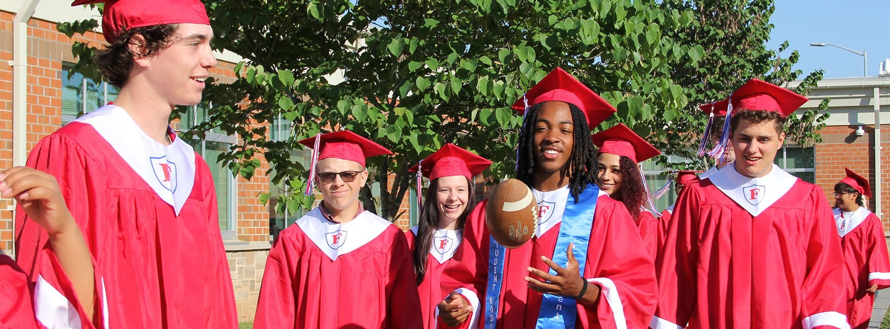 students in graduation caps and gowns. One student tossing a football