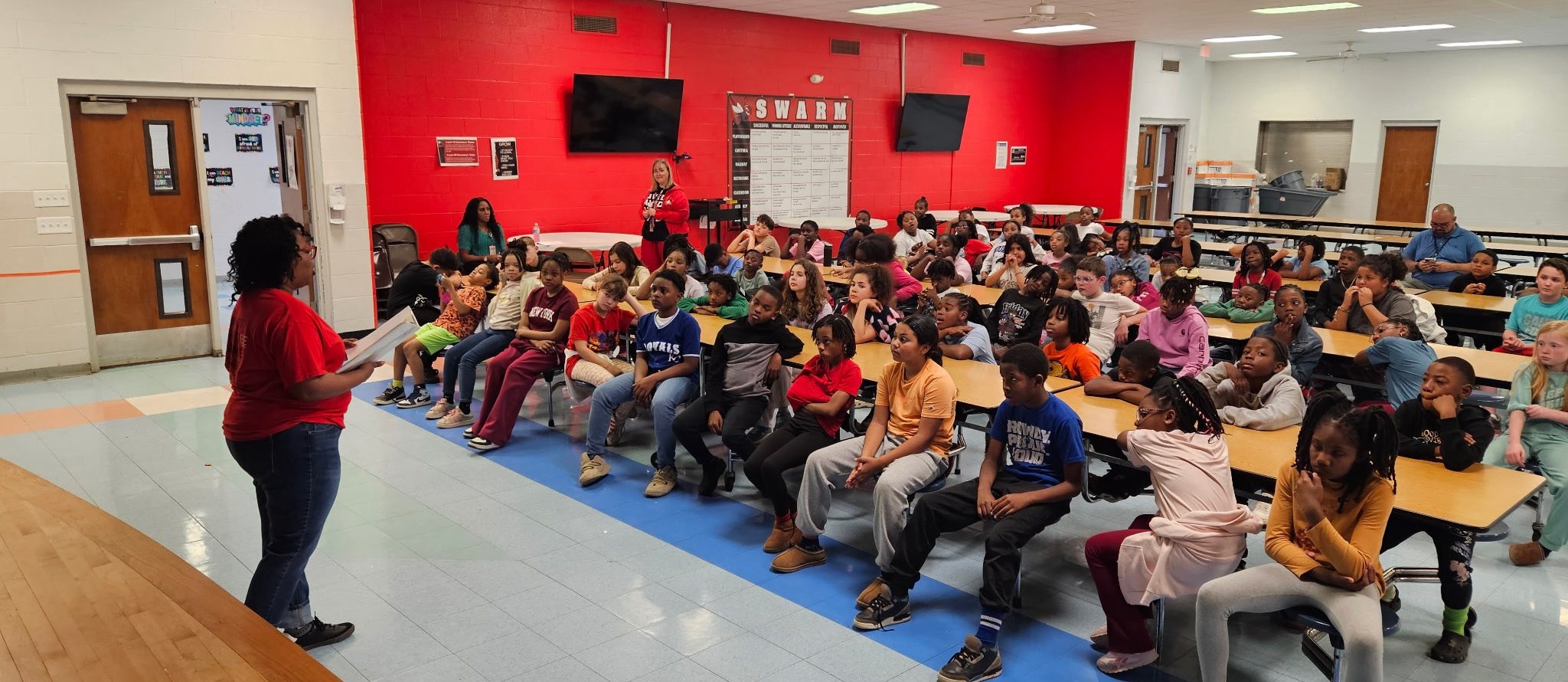 Crystal Hill MAR Slider students sitting in a cafeteria all facing a speaker in a red shirt.