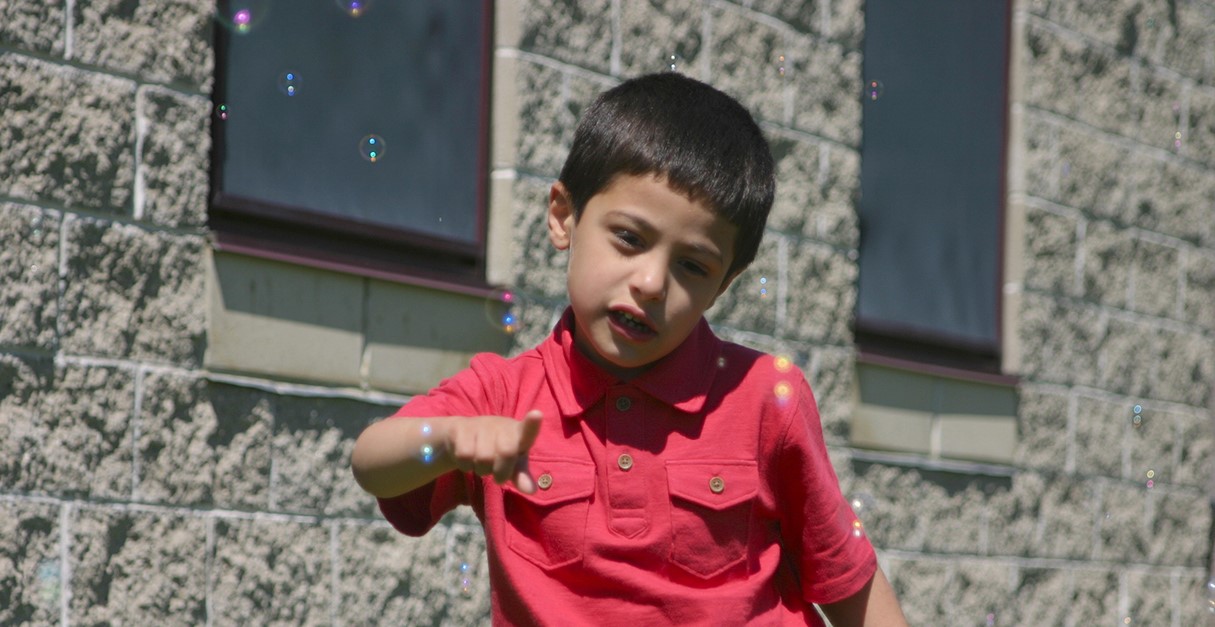 A young boy outside popping bubbles with his finger