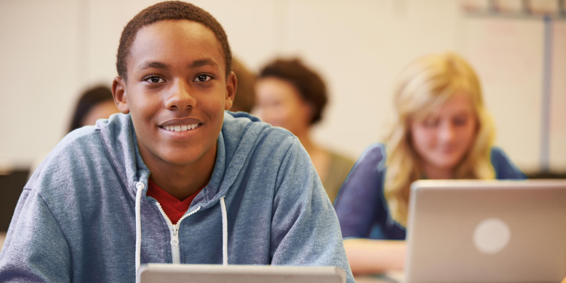 students sitting in a classroom smiling in front of laptops