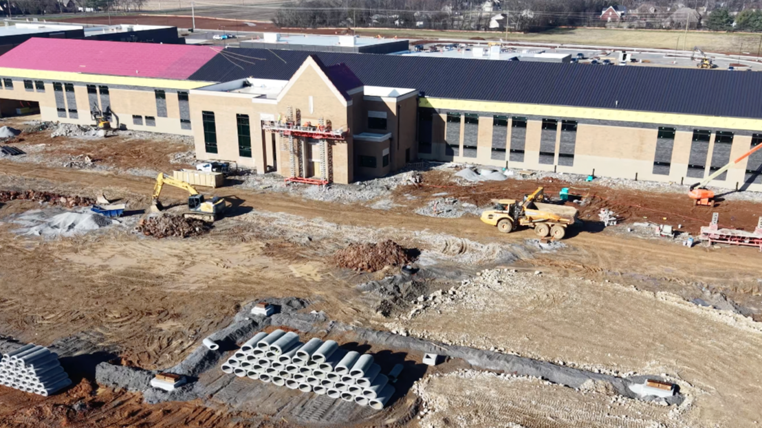 Aerial view of a construction site with a building under construction, a red roof, and heavy machinery.