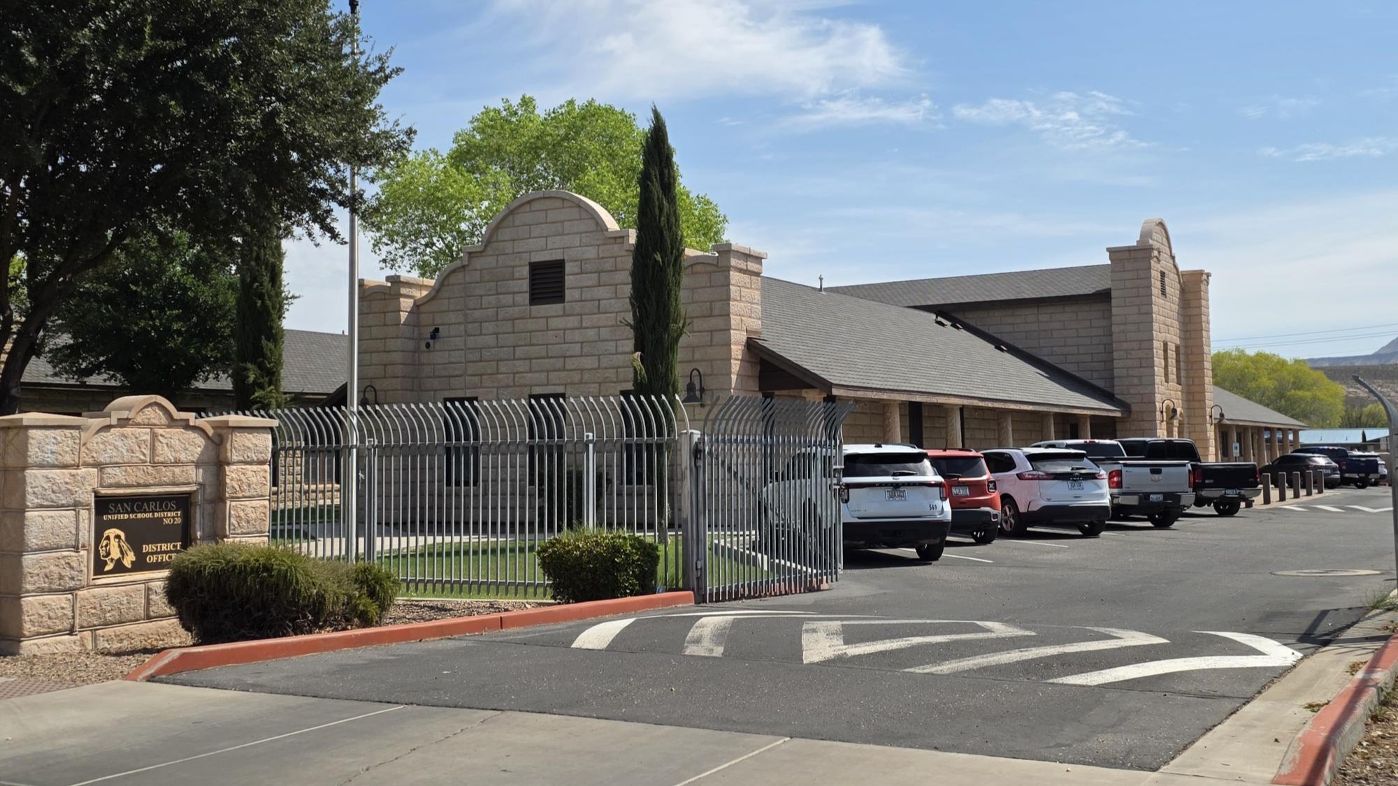 Building with arched entrance and parked cars. Trees and shrubs near the entrance. Road with white arrow.