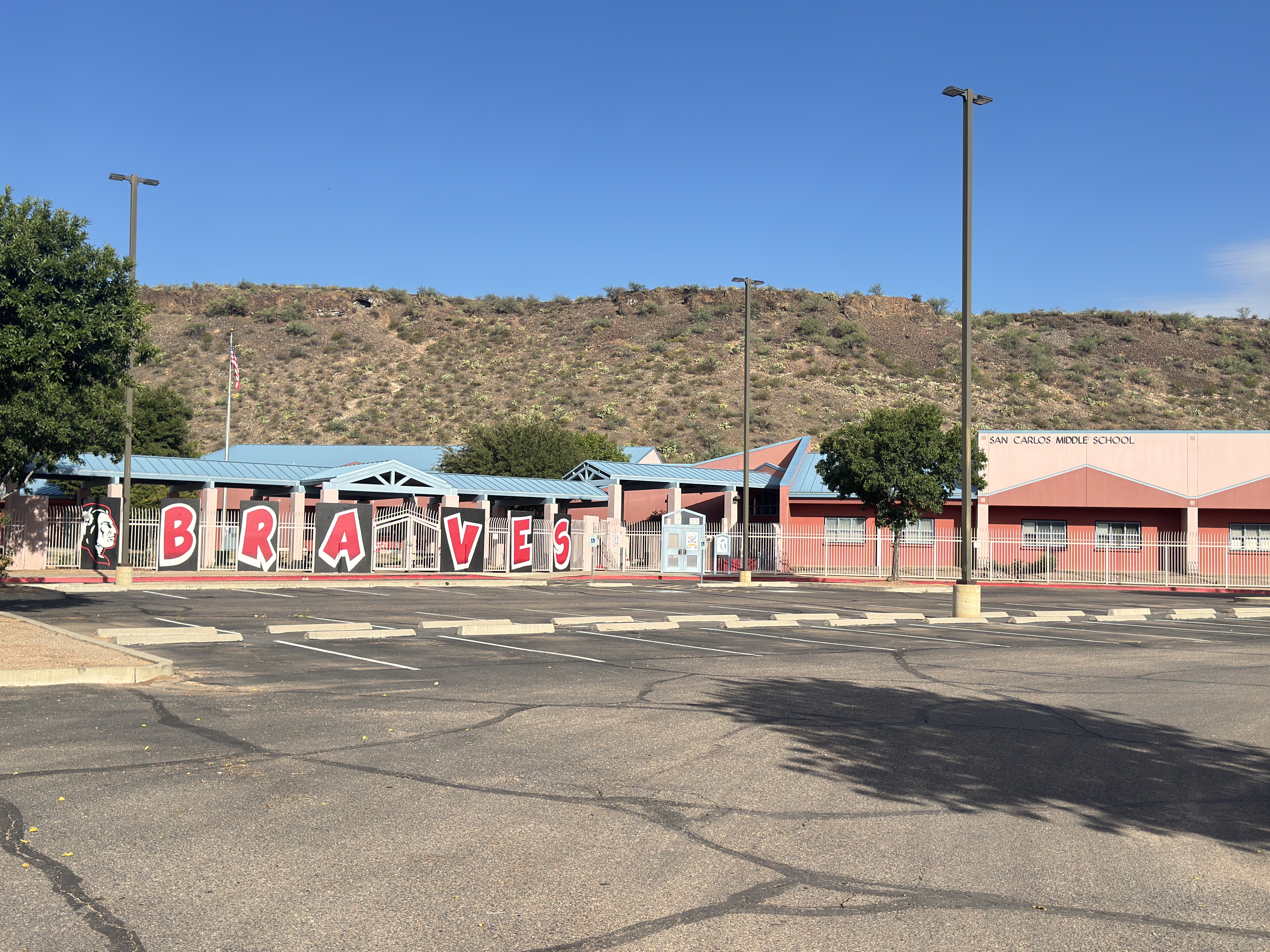 Empty parking lot with street lights, a building reading "BRAVES," and a hill in the background.