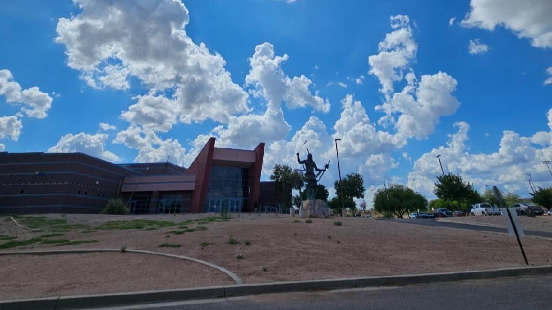 A building with a red roof and large windows under a blue sky with clouds. A statue stands in the foreground.