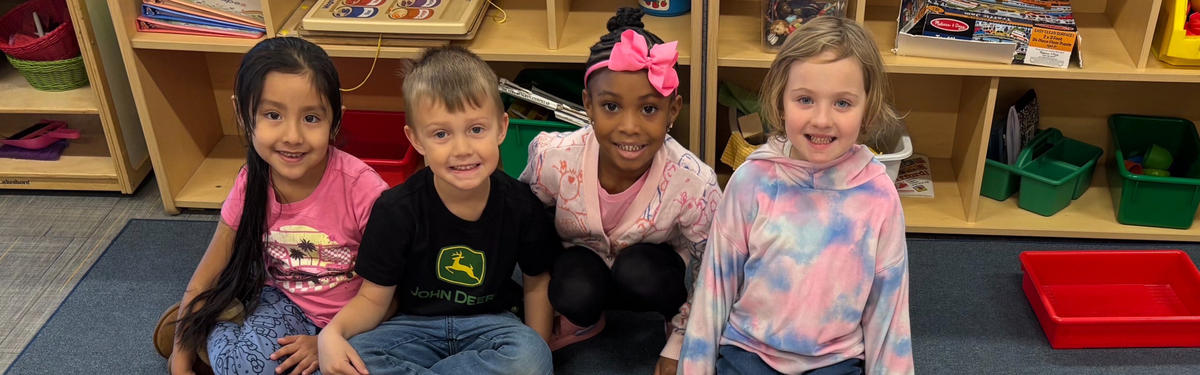 A group of four children seated on the floor, engaged in an early childhood classroom