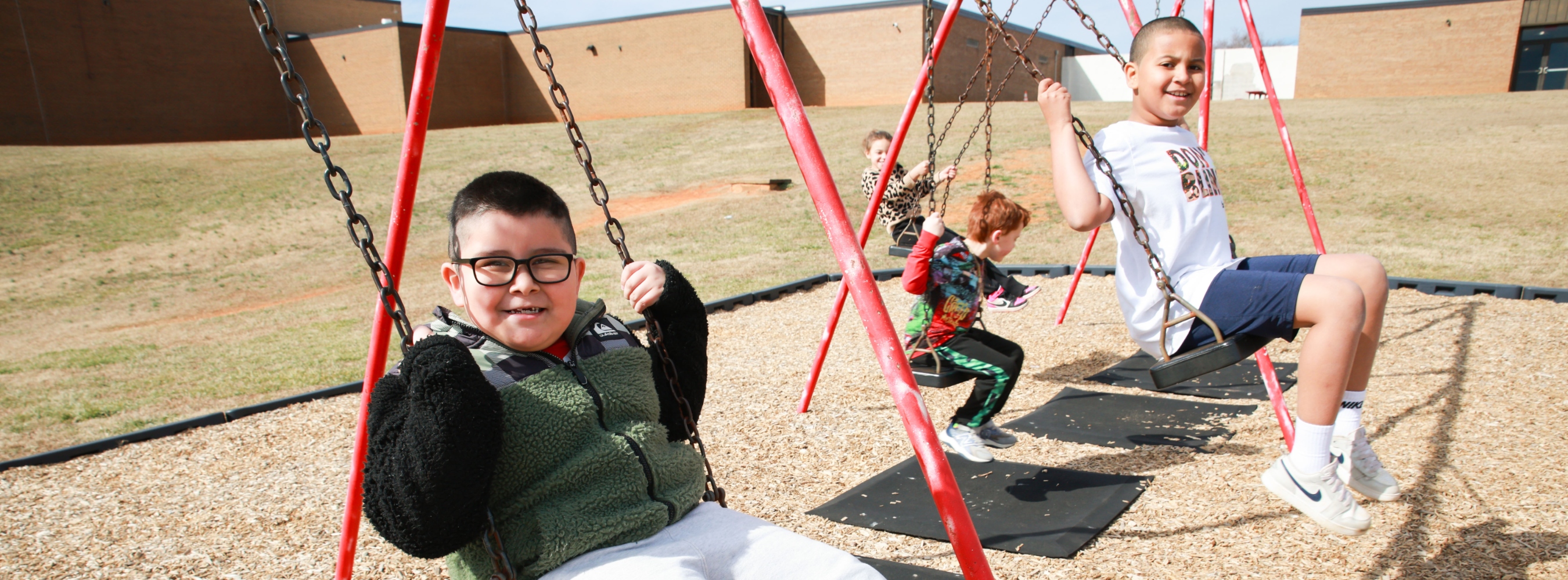 Mayo Elementary School students are outside on the swings smiling.