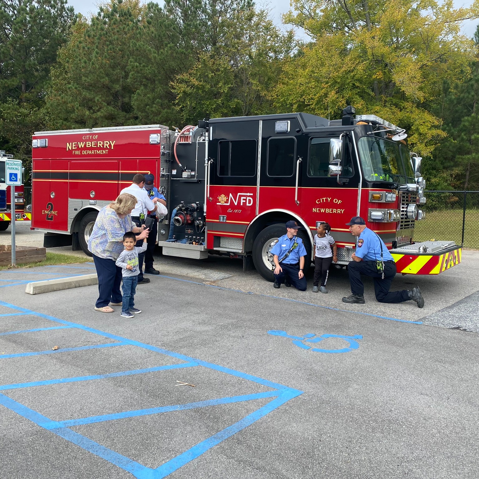 Firefighters interacting with young children in front of the Newberry Fire Department fire truck.