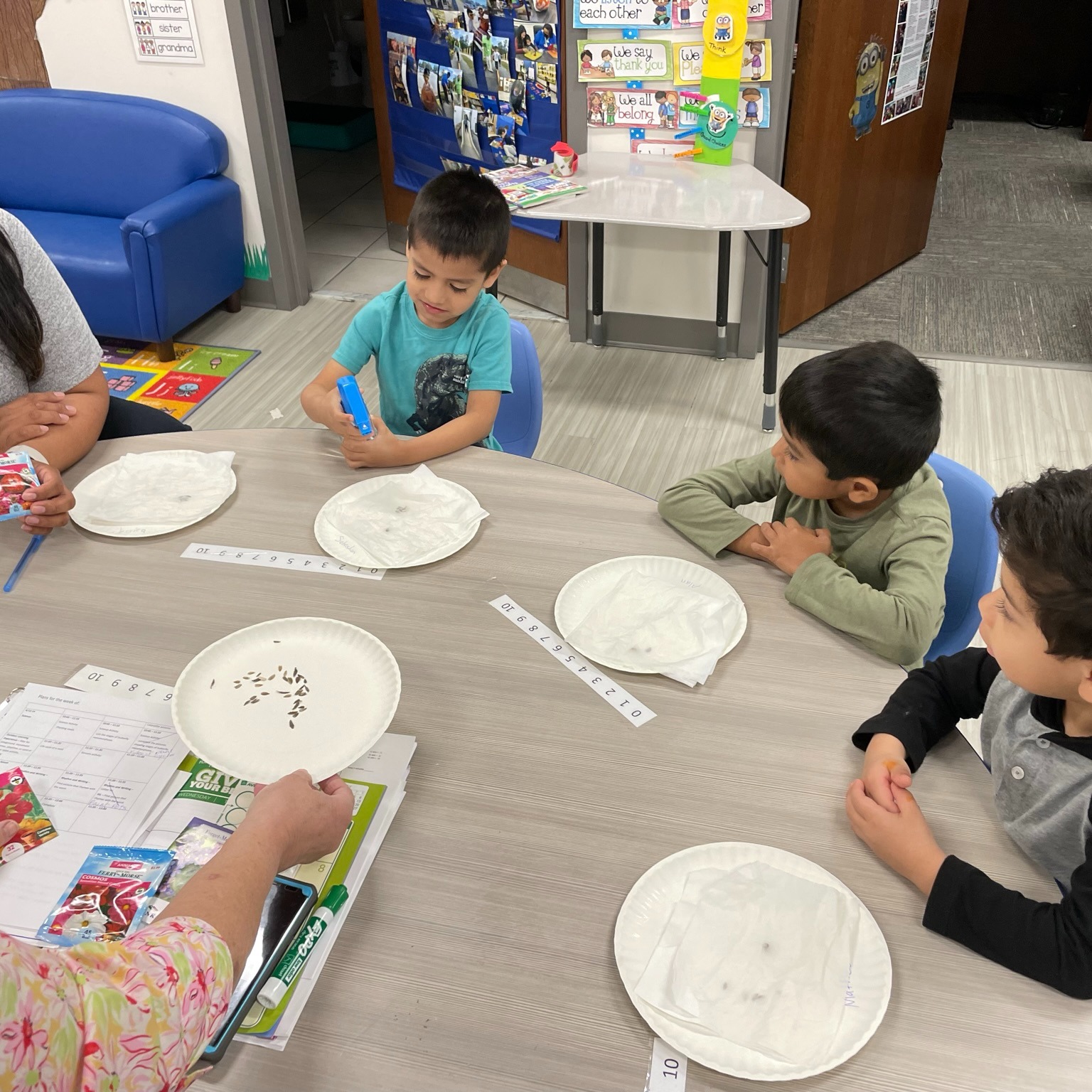 Children and a woman seated at a table with items for an activity in a classroom.