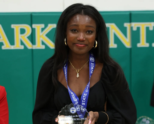 A student smiles while holding an Award of Excellence trophy at a state championship.