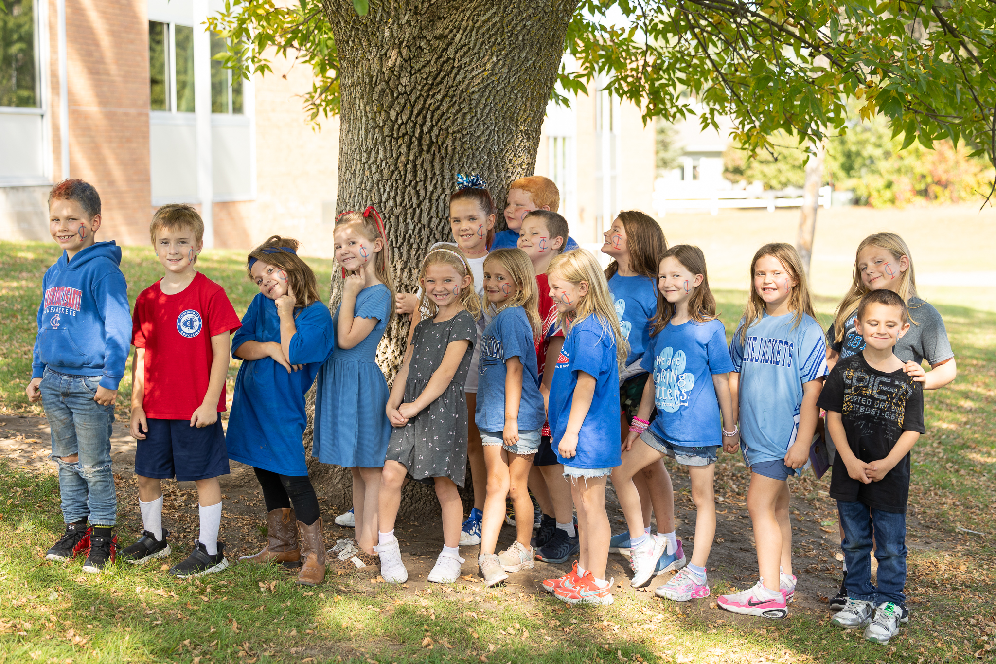 A large group of elementary school students smile and pose together by a tree during a school spirit event.