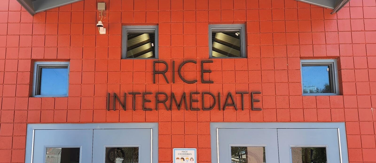 A red building with "RICE INTERMEDIATE" in white above two blue doors. Two windows are on either side of the text.