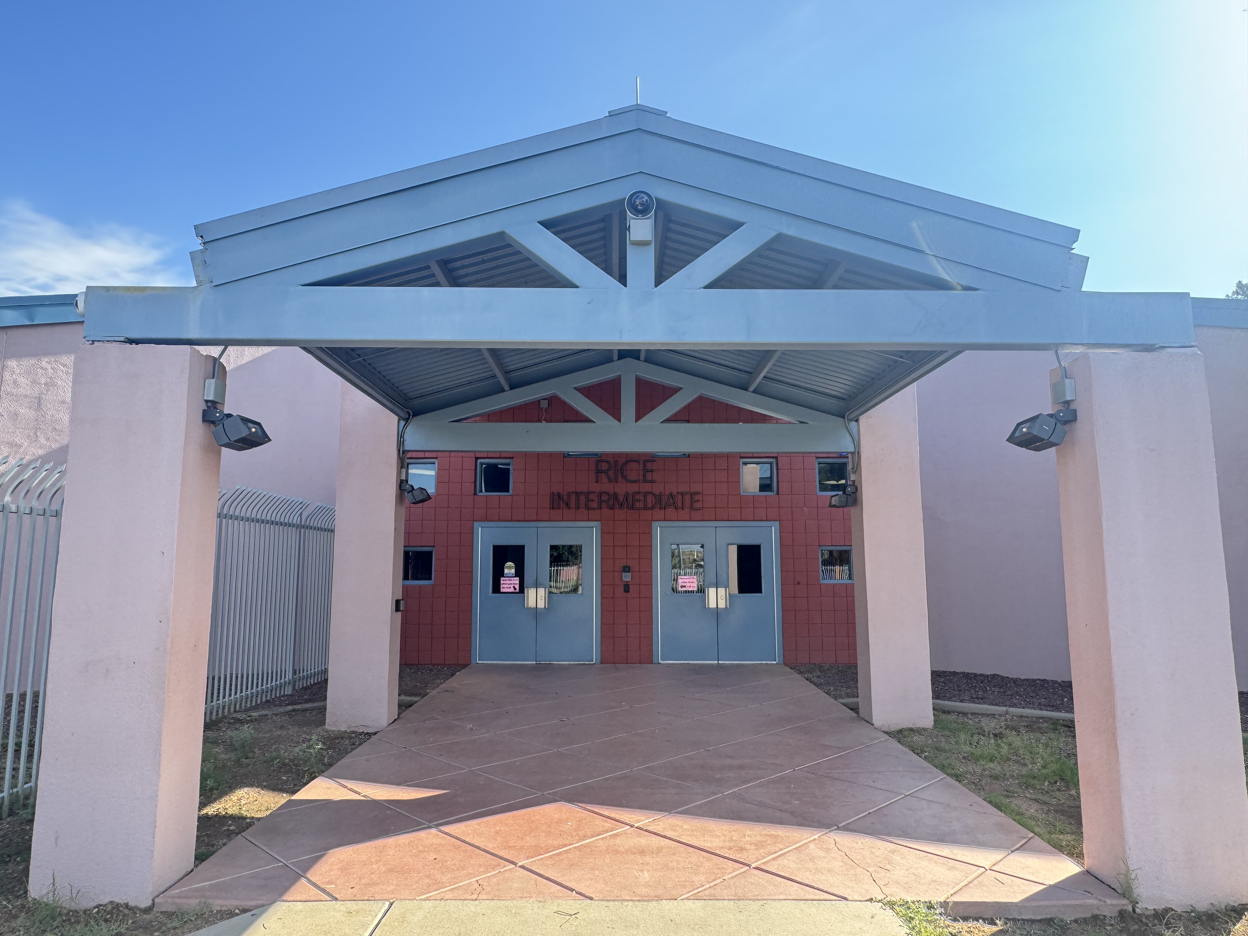 Entrance to a building with a blue awning and three doors. The walls are red and pink.