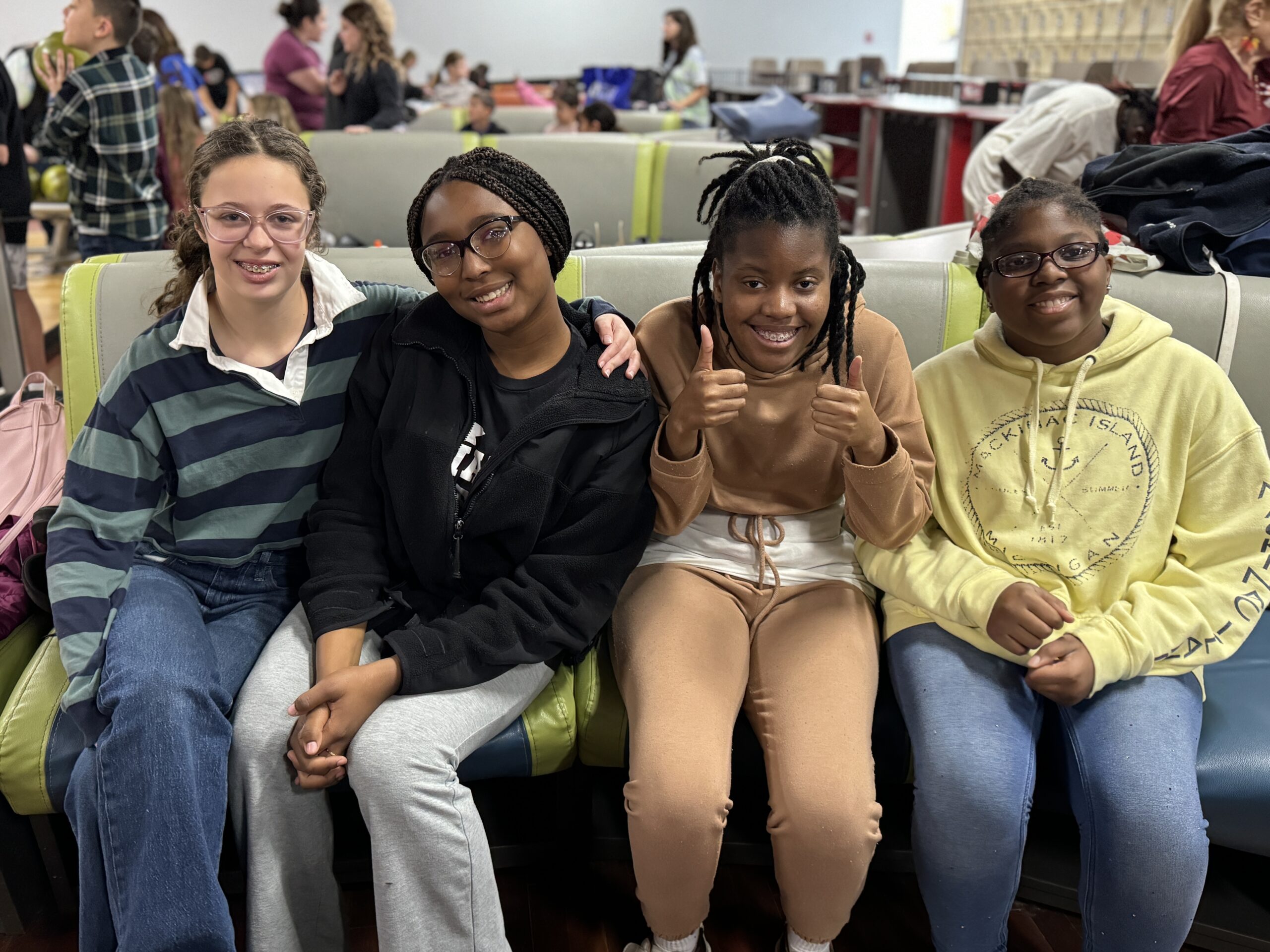 Four girls sit on a bench in a cafeteria, smiling and posing for a photo.