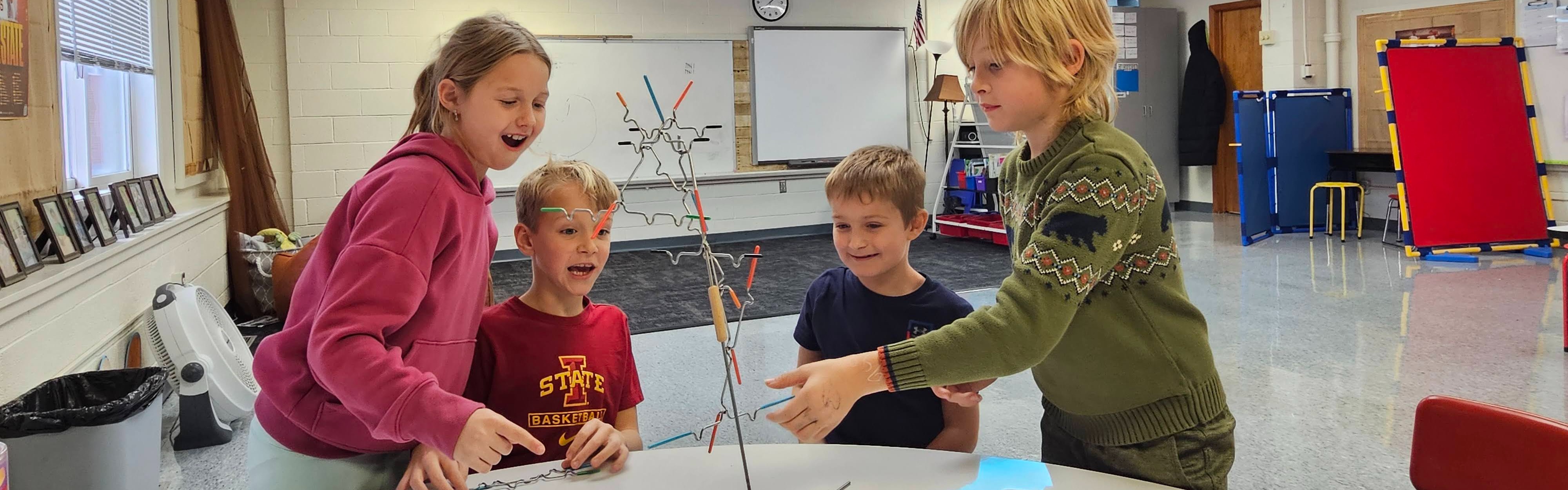 Students building a popsicle stick tower at a classroom table
