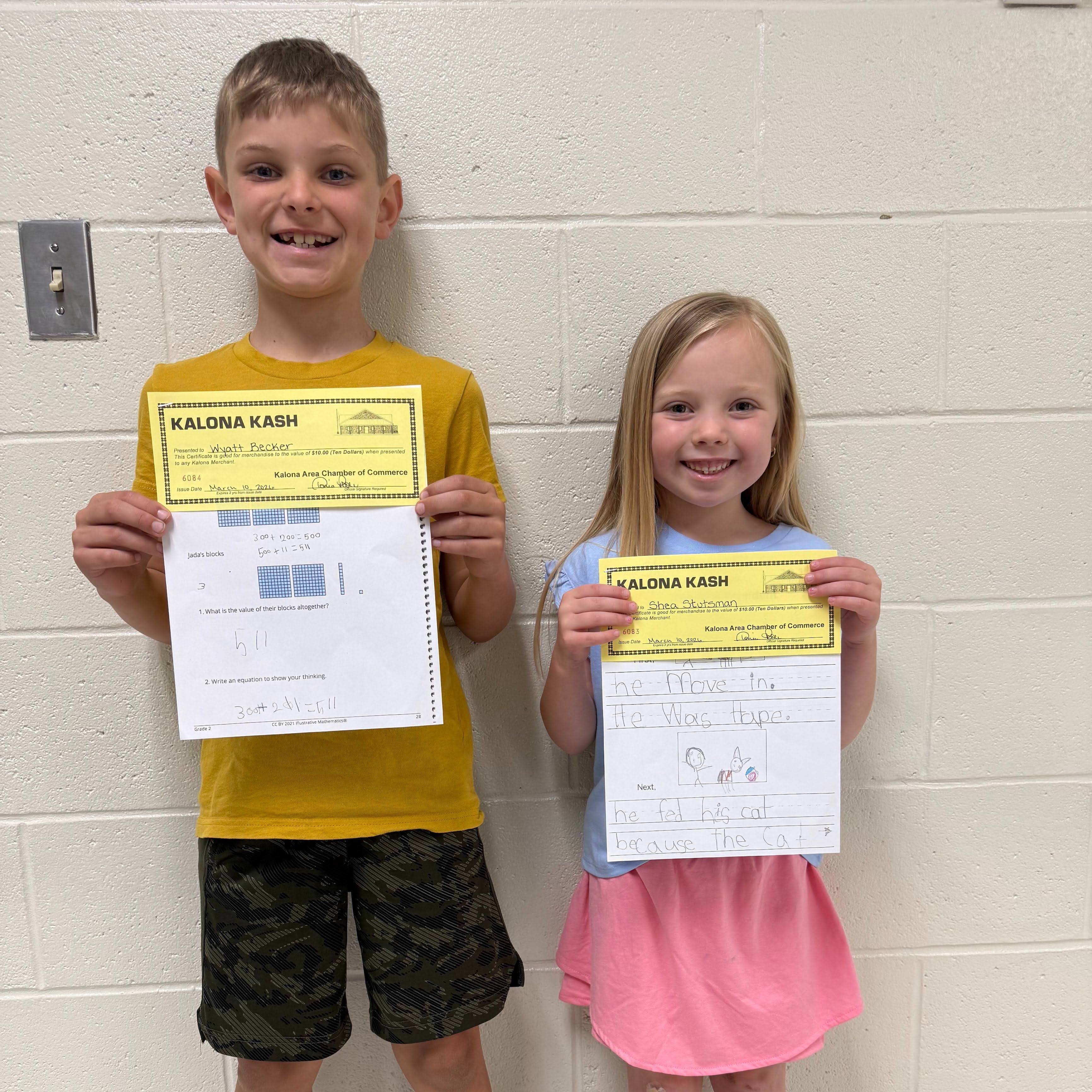 Two students holding up their academic awards; text on award says Kalona Cash