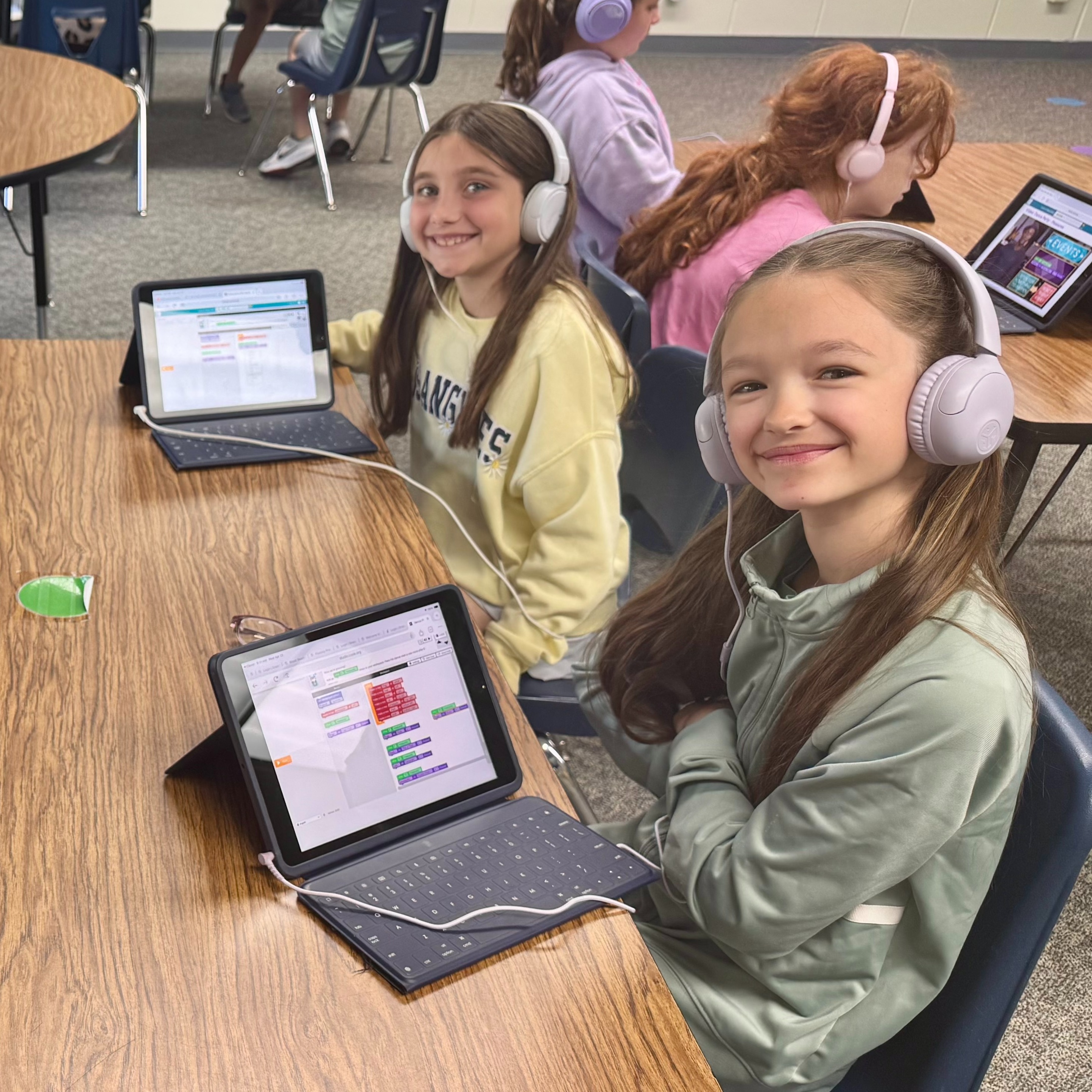 Students sitting at tables with ipads working on a coding application wearing headphones plugged into each ipad